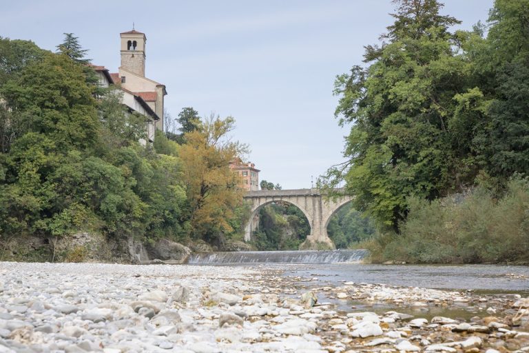 rivière avec plage de galets et arbres devant pont